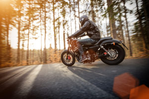 Man Riding On Motorcycle On Road In Sunny Forest