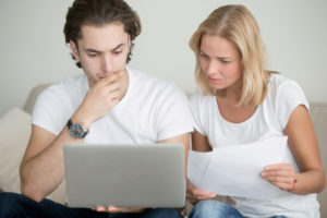 Man And Woman Holding Papers Intently Looking At Computer