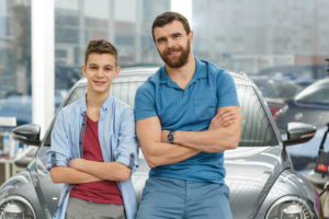 Father And Teenage Son Standing In Front Of Car